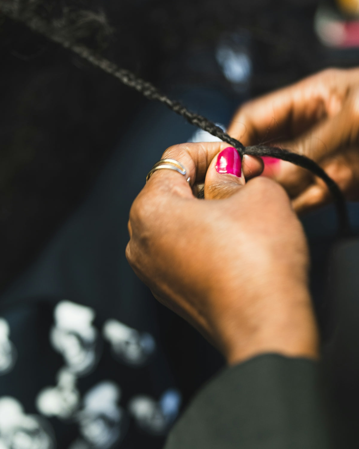 Hands braiding hair with pink fingernails