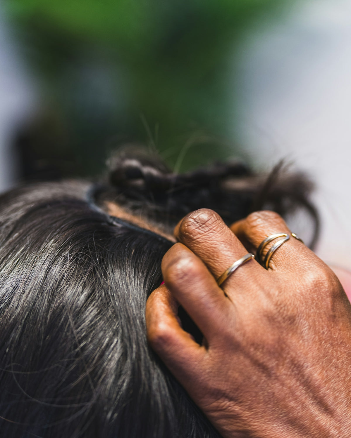 A hand braiding dark hair with rings.