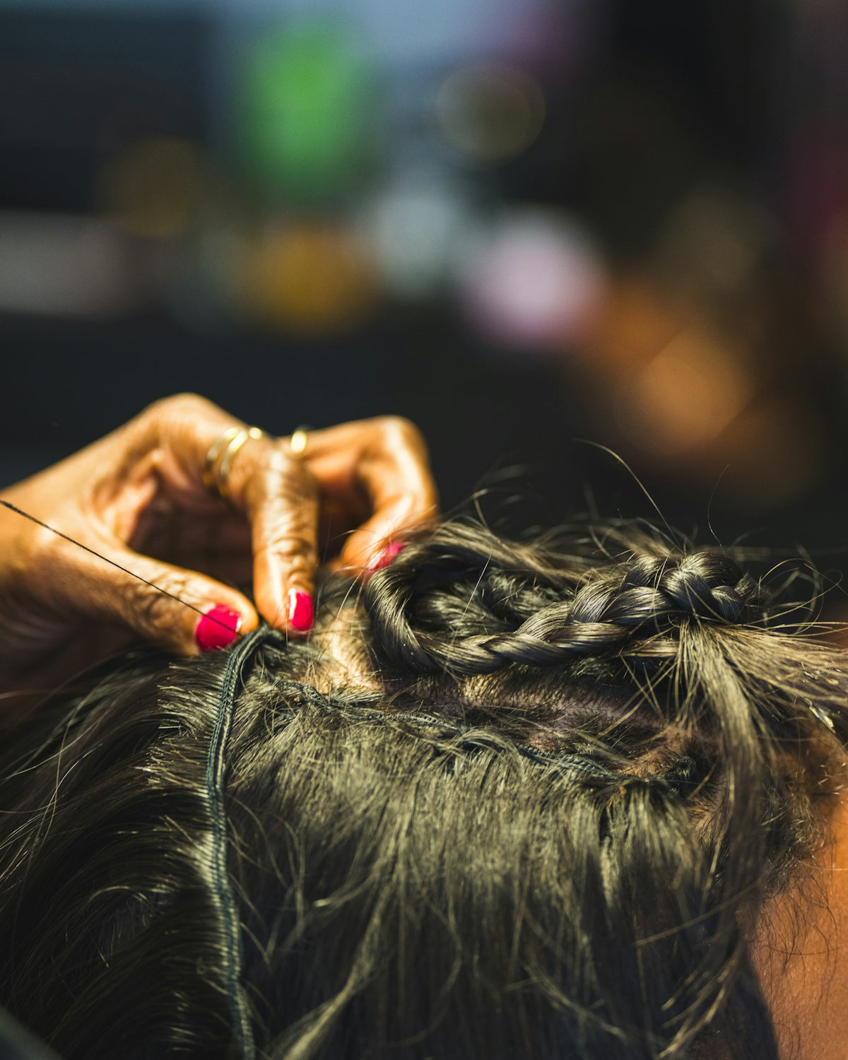 Braids being sewn into dark hair by a manicured hand.