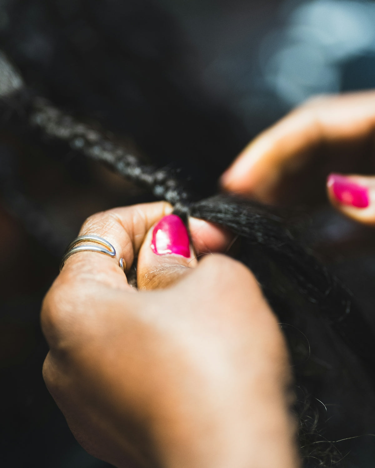 Hands braiding dark, long hair with pink nails.